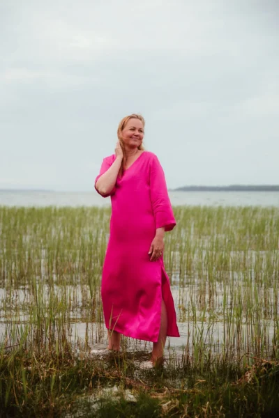 Naine kannab erksat roosat viskoosist suvekleiti looduses – avara lõikega kleit, mis on osa Eesti disainist ja valmistatud Muhumaal.